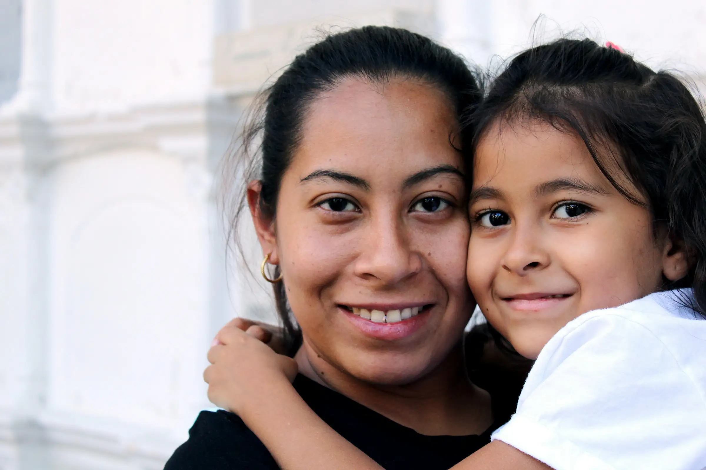 Una mujer y una niña abrazadas mejilla con mejilla, sonriendo